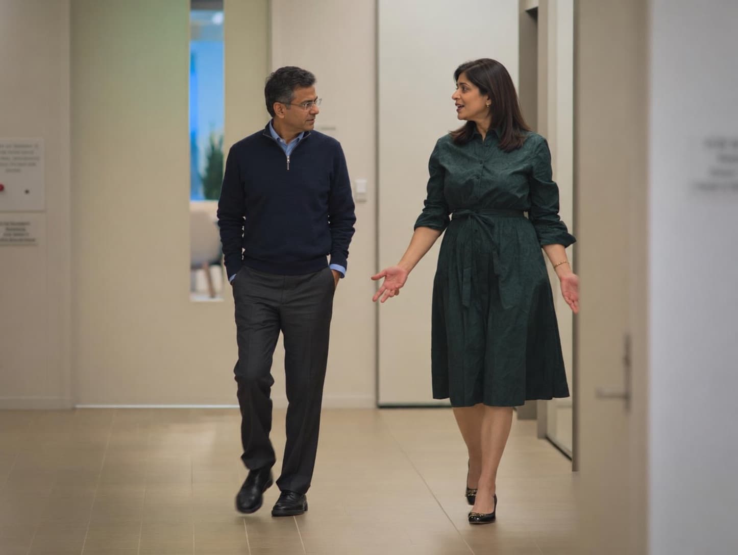 Two coworkers talking as they walk down an office corridor