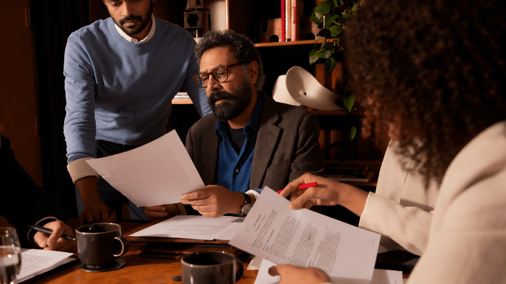 People around a wooden table in a warmly lit office, going through documents together